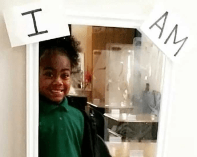 A young girl smiling at her reflection in a mirror with a "Positivity Picture" nearby, illustrating the connection between emotional well-being and reading confidence.