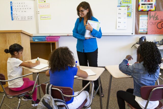 A teacher working with a small group of students at a table, modeling a "learning to read" lesson using explicit instruction.