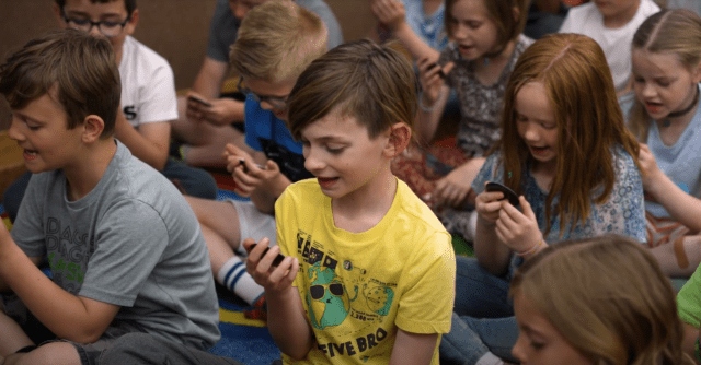 A student looking into a small handheld mirror to observe their mouth and tongue placement while practicing phonetic articulation.