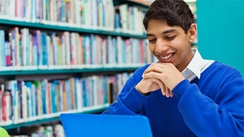 A multilingual learner smiling as he looks at his computer screen.