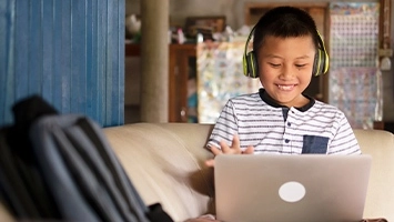 A young student wearing headphones, engaged in remote learning on a laptop.
