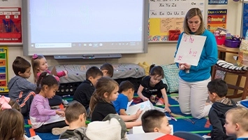 A Kindergarten class sitting on the floor engaged in a dictation activity.