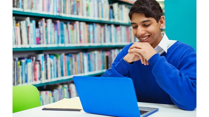 A multilingual learner smiling as he looks at his computer screen.