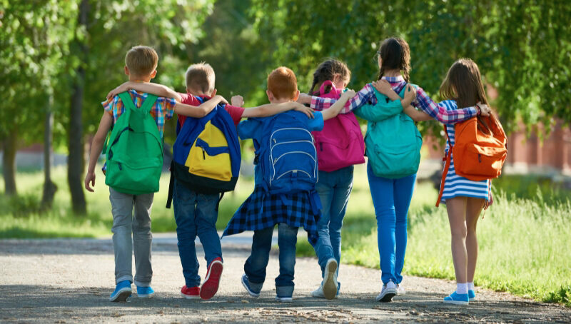 6 students walking arm in arm down a road wearing backpacks