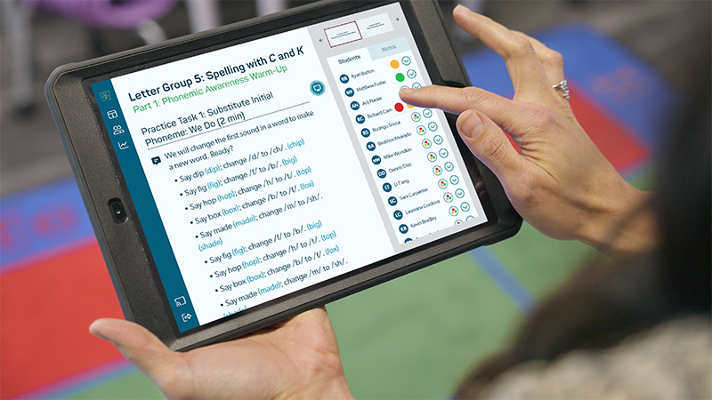 A close-up view of an iPad screen displaying a lesson script from the New Reading Horizons Discovery instructional software. The teacher is tapping an observation status for one of her students.