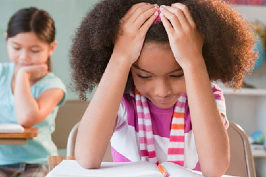 A young student with her hands on her head, appearing focused and determined while she continues to struggle with difficult words during an accountable reading exercise.