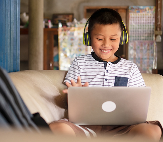 A young student wearing headphones, engaged in remote learning on a laptop.