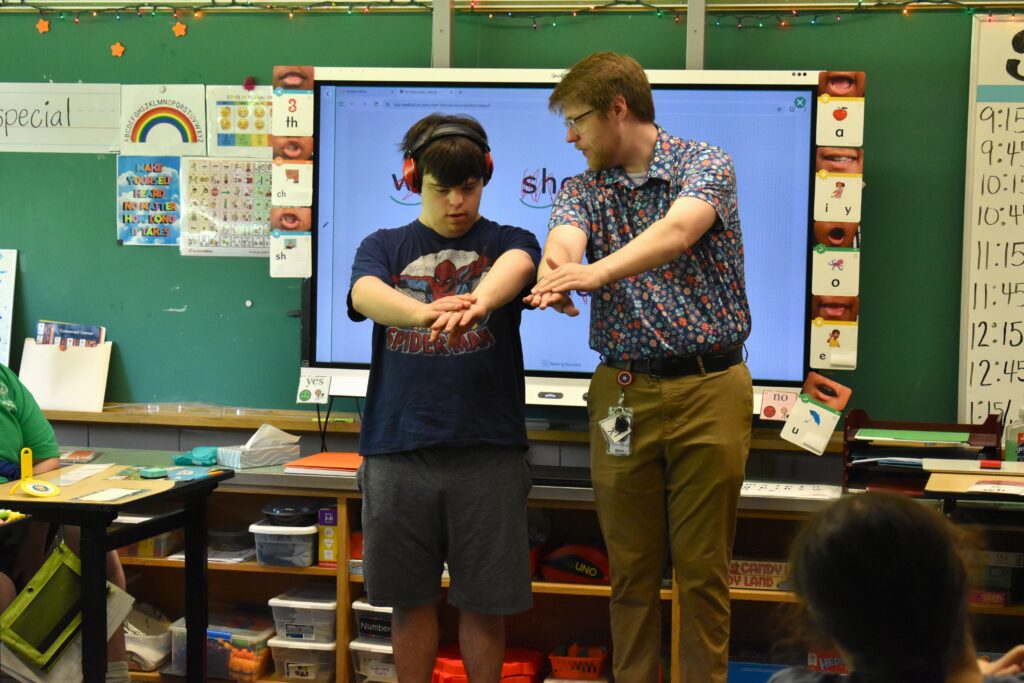 Teacher uses his arms to demonstrate how to sound out letters to student with intellectual and developmental disabilities.