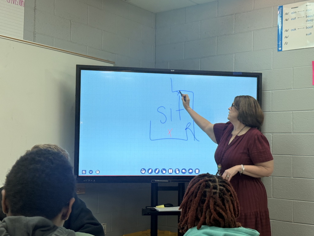 Teacher marking and decoding a word on an interactive display while guiding students through explicit phonics instruction.