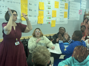 Teacher leading an interactive literacy lesson as secondary students participate in phonics and word analysis with hand motions and classroom discussion.